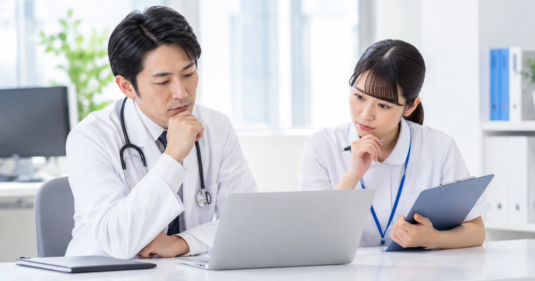 診療室でノートパソコンと手元の資料を確認する医師と看護師
